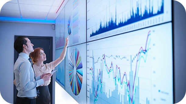 a man and woman looking at a large screen with graphs